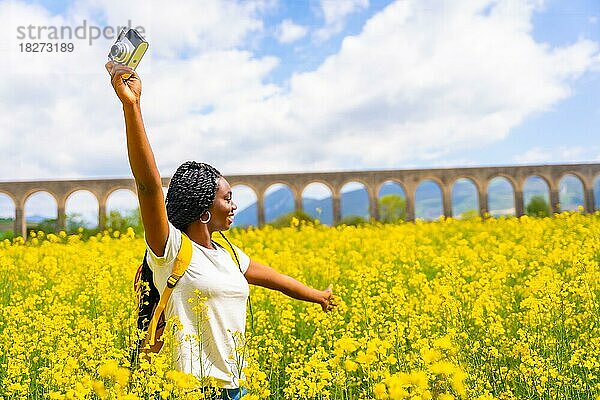 Freiheitsgefühle mit der Kamera  ein schwarzes ethnisches Mädchen mit Zöpfen  eine Reisende  in einem Feld mit gelben Blumen