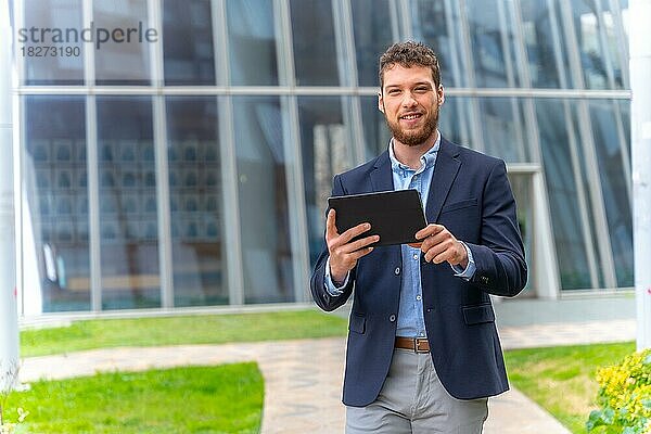 Junger männlicher Geschäftsmann oder Unternehmer außerhalb des Büros  der mit einem Tablet in der Hand geht