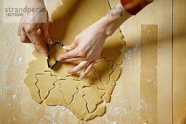 Draufsicht auf eine Frauenhand  die mit einer Ausstechform Kekse aus dem Teig ausschneidet