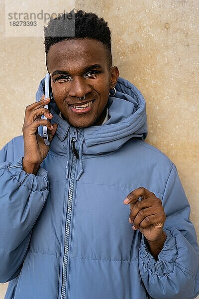 Porträt eines schwarzen ethnischen Mannes mit einem Telefon und einer blauen Jacke auf gelbem Hintergrund  der telefoniert