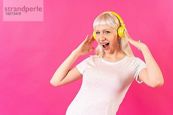 Blondes kaukasisches Mädchen im Studio auf rosa Hintergrund  lächelnd  hört Musik mit Kopfhörern