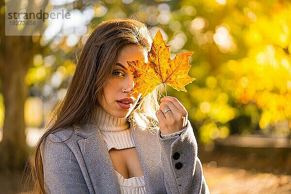 Eine hübsche Frau genießt den Herbst in einem Park bei Sonnenuntergang und zeigt ein Blatt von einem Baum