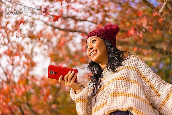 Porträt einer asiatischen Frau im Herbst mit einem Handy  die eine Sprachnachricht in einem Wald aus roten Blättern sendet  Technik