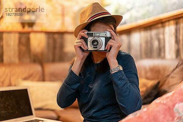 Eine hübsche Touristin mit Hut und Fotoapparat trinkt eine Tasse Tee in einem Café und macht Fotos mit der alten Kamera