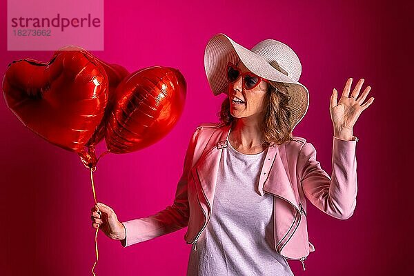 Porträt einer kaukasischen Frau  die mit einem weißen Hut in einem Nachtclub mit einigen Herzluftballons tanzt  rosa Hintergrund