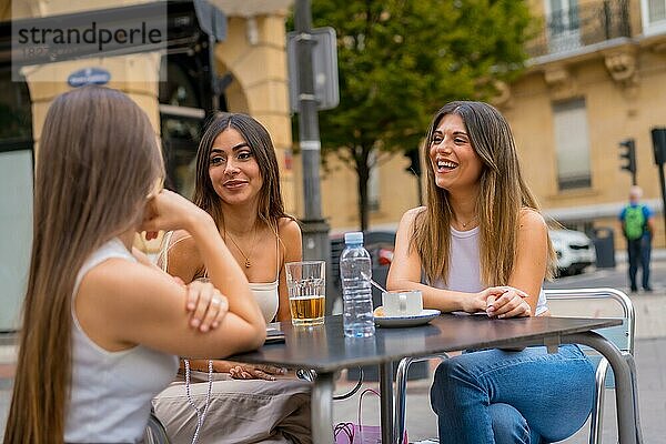 Porträt junger Freundinnen  die an einem Nachmittag auf der Terrasse einer Cafeteria im Herbst etwas trinken