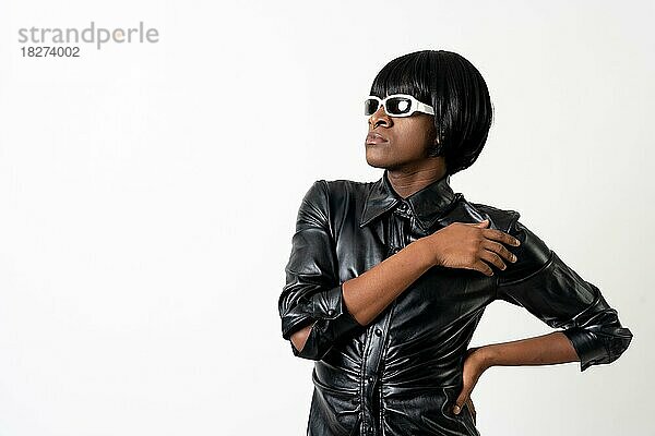 Schwarzer ethnischer Mann im Studio mit weißem Hintergrund  LGTBI Konzept  trägt Leder  Sonnenbrille und Perücke
