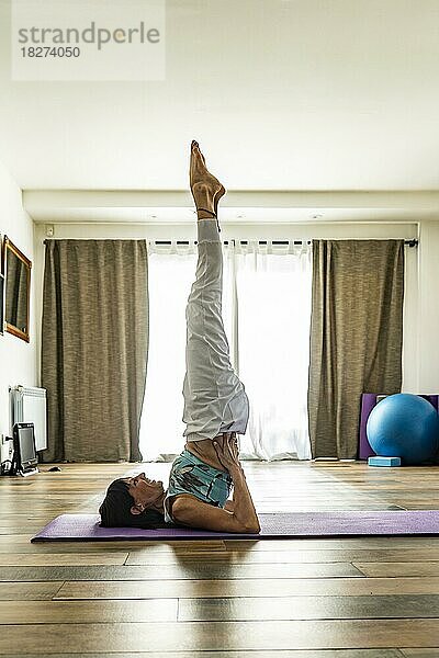 Seitenansicht einer Yogapraktizierenden  die die Schulterstand-Pose einnimmt. Yoga-Studio