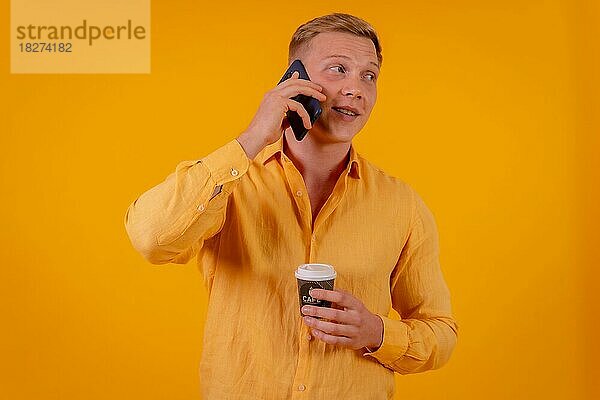 Blonder kaukasischer Mann auf gelbem Hintergrund  der einen Anruf mit dem Telefon tätigt