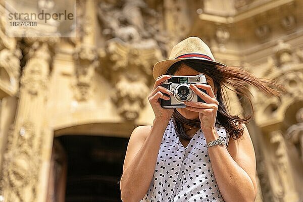 Eine Frau mit Hut  die die Stadt besichtigt und Fotos mit einer alten Kamera macht  die Sommerferien genießend  Konzept einer weiblichen Reisenden und Schöpferin digitaler Inhalte