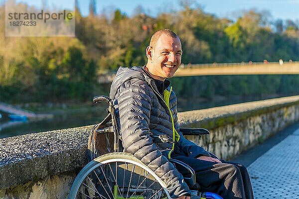 Porträt einer behinderten Person im Rollstuhl  die neben einem Fluss in einem Park lächelt