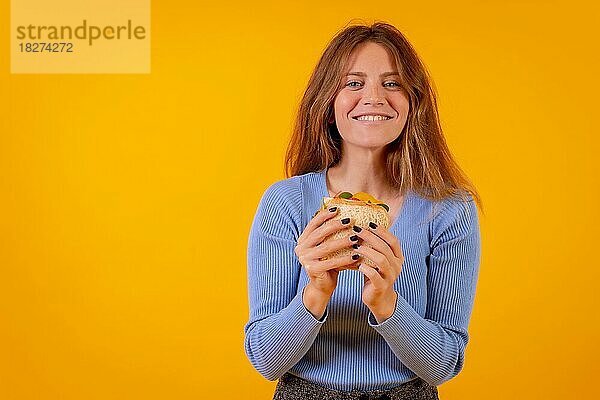 Porträt einer Frau  die ein Sandwich auf gelbem Hintergrund isst  gesundes und vegetarisches Essen