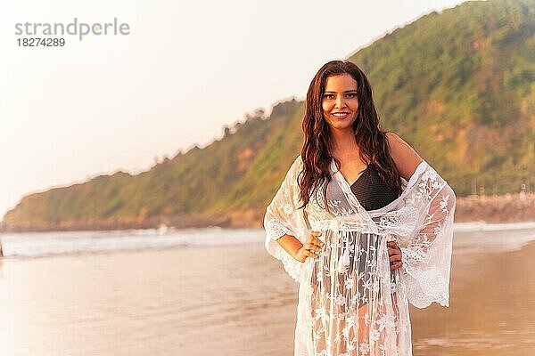 Porträt einer Frau bei Sonnenuntergang in einem weißen Kleid  die den Sommer am Strand genießt