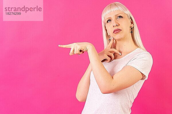 Blonde kaukasische Mädchen Studio Schuss auf rosa Hintergrund  Kopie Raum  nachdenklich zeigt nach links