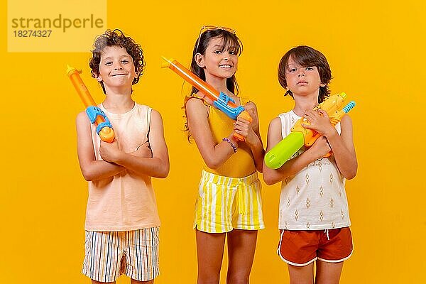 Kinder mit Wasserpistolen im Sommerurlaub  gelber Hintergrund