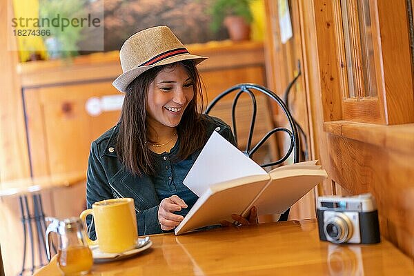 Ein Touristenmädchen mit einer Fotokamera trinkt Tee auf der Terrasse einer Cafeteria. Sie liest ein Buch