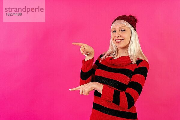 Blondes kaukasisches Mädchen auf rosa Studiohintergrund  Winterthema  lächelnd nach links zeigend  Kopierraum