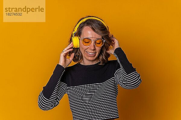 Kaukasisches Mädchen hört Musik  lächelt und tanzt mit ihrem Telefon  Kopfhörer und Sonnenbrille  gelber Hintergrund