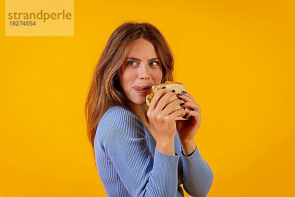 Porträt einer fröhlichen Frau  die ein Sandwich auf einem gelben Hintergrund isst  gesundes und vegetarisches Essen