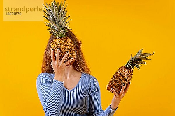 Frau mit einer Ananas mit Sonnenbrille  mit der Ananas in der Mitte geschnitten  gelber Hintergrund