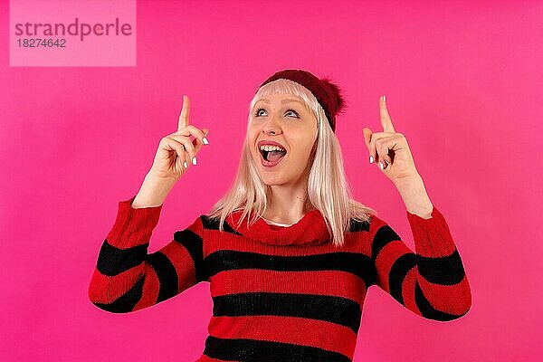 Blonde kaukasische Mädchen auf rosa Hintergrund Studio  Winter-Thema  lächelnd nach oben zeigen