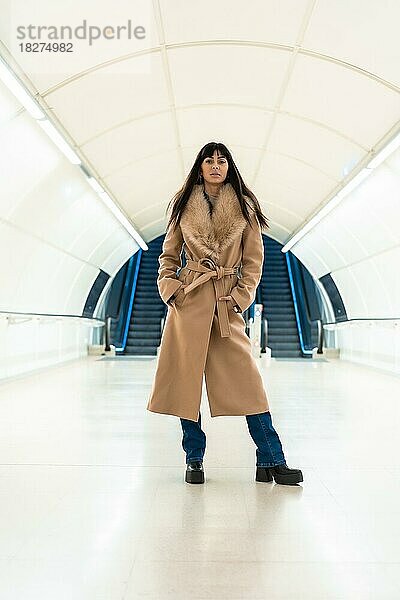 Brünettes Mädchen steigt im Winter mit einer Jacke in die U-Bahn ein. Hübsche Kaukasierin geht durch den Tunnel