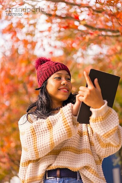 Asiatisches Mädchen  das im Herbst mit einem Tablet in der Hand in einem Wald aus roten Blättern spazieren geht  Technologiekonzept