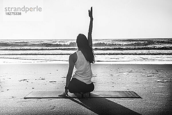 Rückansicht einer jungen Frau  die am Strand Yoga übt. Schwarz-Weiß-Fotografie