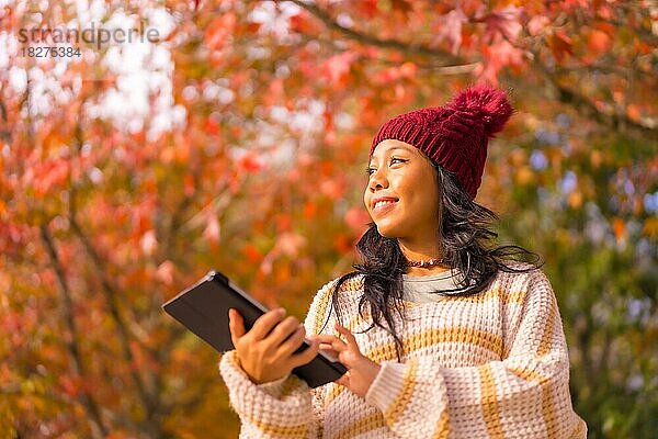 Asiatisches Mädchen im Herbst mit einer Tablette lächelnd in einem Wald von roten Blättern  Technologie-Konzept
