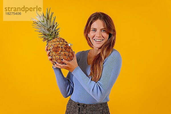 Mädchen lächelnd mit einer Ananas in Sonnenbrille in einem Studio auf einem gelben Hintergrund  gesund  Sommer