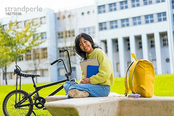 Porträt einer lächelnden asiatischen Studentin  die auf einem College-Campus mit einem Fahrrad sitzt