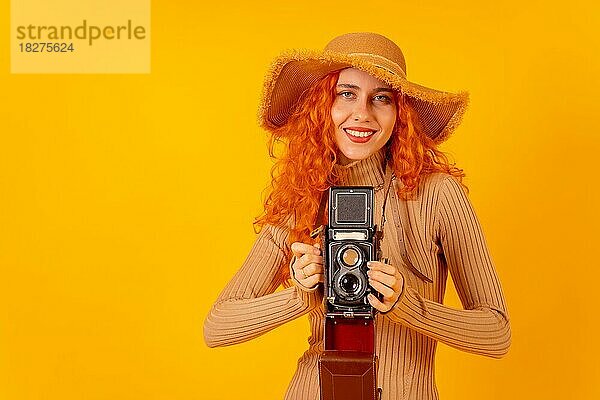Rothaarige Touristin auf gelbem Hintergrund  Studioaufnahme  mit einer alten Fotokamera