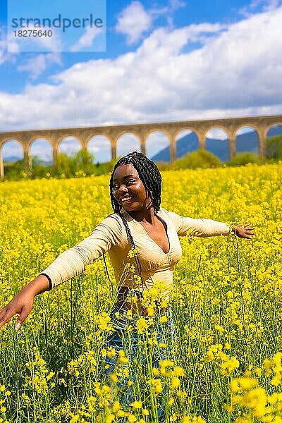 Lifestyle  lächelnd die Natur genießen  Porträt eines schwarzen ethnischen Mädchens mit Zöpfen  Reisende  in einem Feld mit gelben Blumen