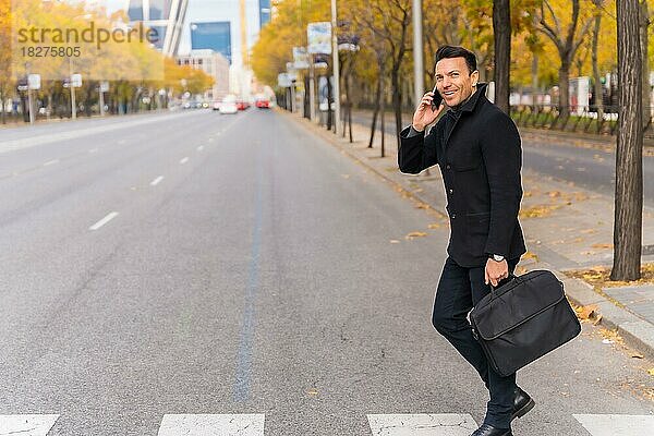 Kaukasischer Geschäftsmann mittleren Alters  der auf dem Weg zur Arbeit telefoniert und die Straße überquert