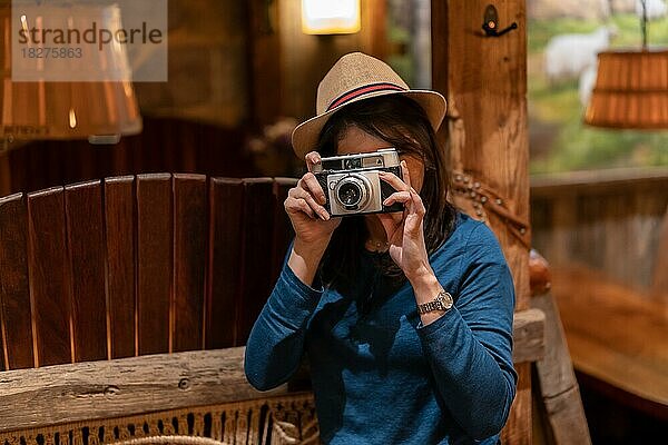 Eine hübsche Touristin mit Hut und Fotoapparat trinkt Tee in einem Café und macht ein paar Fotos mit der alten Kamera