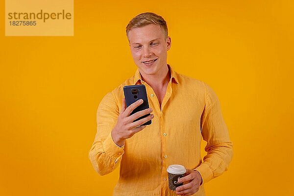 Blonder kaukasischer Mann auf gelbem Hintergrund  der mit dem Telefon arbeitet