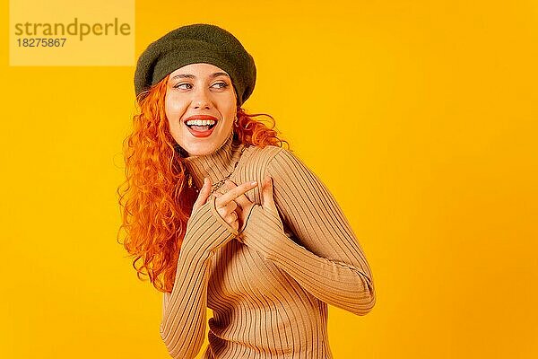 Rothaarige Frau mit Baskenmütze im Studio auf gelbem Hintergrund  Kopierraum  lächelnd und zeigend