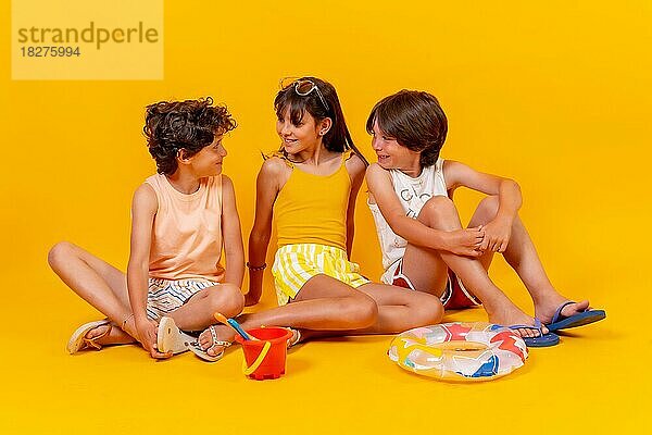 Porträts von Kindern  die auf dem Boden sitzen und die Ferien mit Spielzeug genießen  gelber Hintergrund