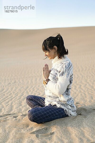 Seitenansicht einer Frau  die sich am Strand an den Händen fasst. Namaste-Pose