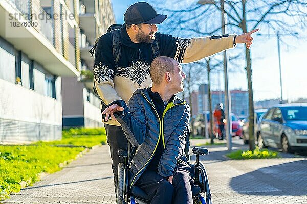 Ein behinderter Mensch im Rollstuhl mit einem Freund  der spazieren geht und Spaß hat - Normalität für Behinderte