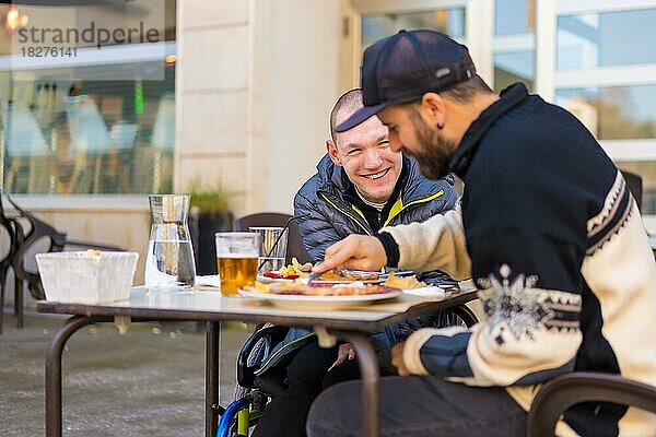 Eine behinderte Person isst und lächelt mit einem Freund  der Spaß hat  Terrasse eines Restaurants