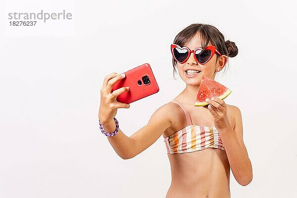 Mädchen mit Sonnenbrille genießt den Sommer  isst eine Wassermelone und macht ein Selfie mit dem Telefon. Weißer Hintergrund