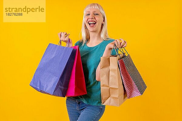 Lachende Einkaufen mit Taschen auf Verkauf  blonde kaukasische Mädchen im Studio auf gelbem Hintergrund