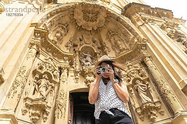 Eine Frau mit Hut  die die Stadt besichtigt und mit einer alten Kamera Fotos macht und den Sommerurlaub genießt  Konzept einer weiblichen Reisenden oder Urlauberin und Erstellerin digitaler Inhalte