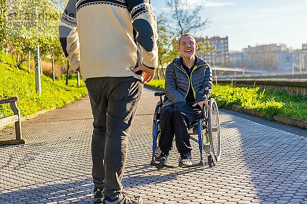 Behinderte Person im Rollstuhl lächelt mit einem Familienmitglied bei einem Spaziergang in einem Park