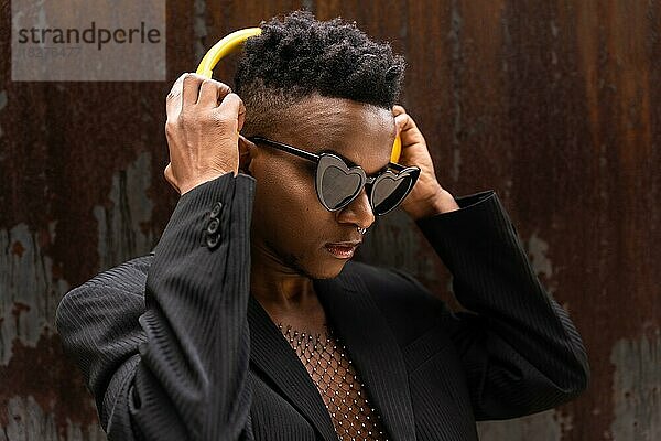 Schwarzer ethnischer Mann  der Musik hört  drahtlose gelbe Kopfhörer  mit Herz-Sonnenbrille  hört moderne Musik
