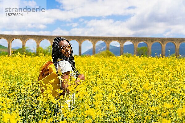 Porträt eines schwarzen ethnischen Mädchens mit Zöpfen  das in die Sonne schaut  Sonnenbrille  Reisende  in einem Feld mit gelben Blumen