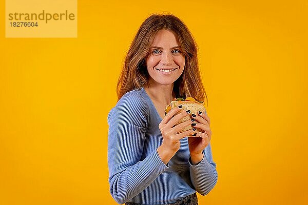 Porträt einer Frau  die ein Sandwich auf gelbem Hintergrund isst  gesundes und vegetarisches Essen