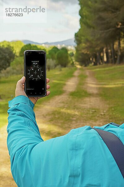 Frau  die sich im Wald mit dem Kompass ihres Smartphones orientiert und einem Pfad im Kiefernwald folgt