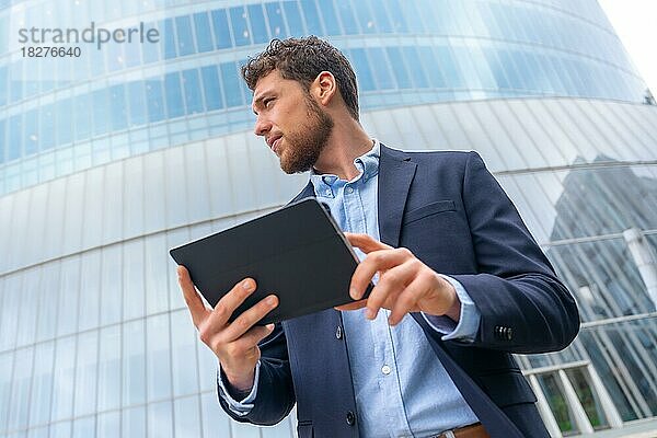 Porträt eines männlichen Geschäftsmannes oder Unternehmers außerhalb des Büros  der ein Tablet in einem Glasgebäude benutzt